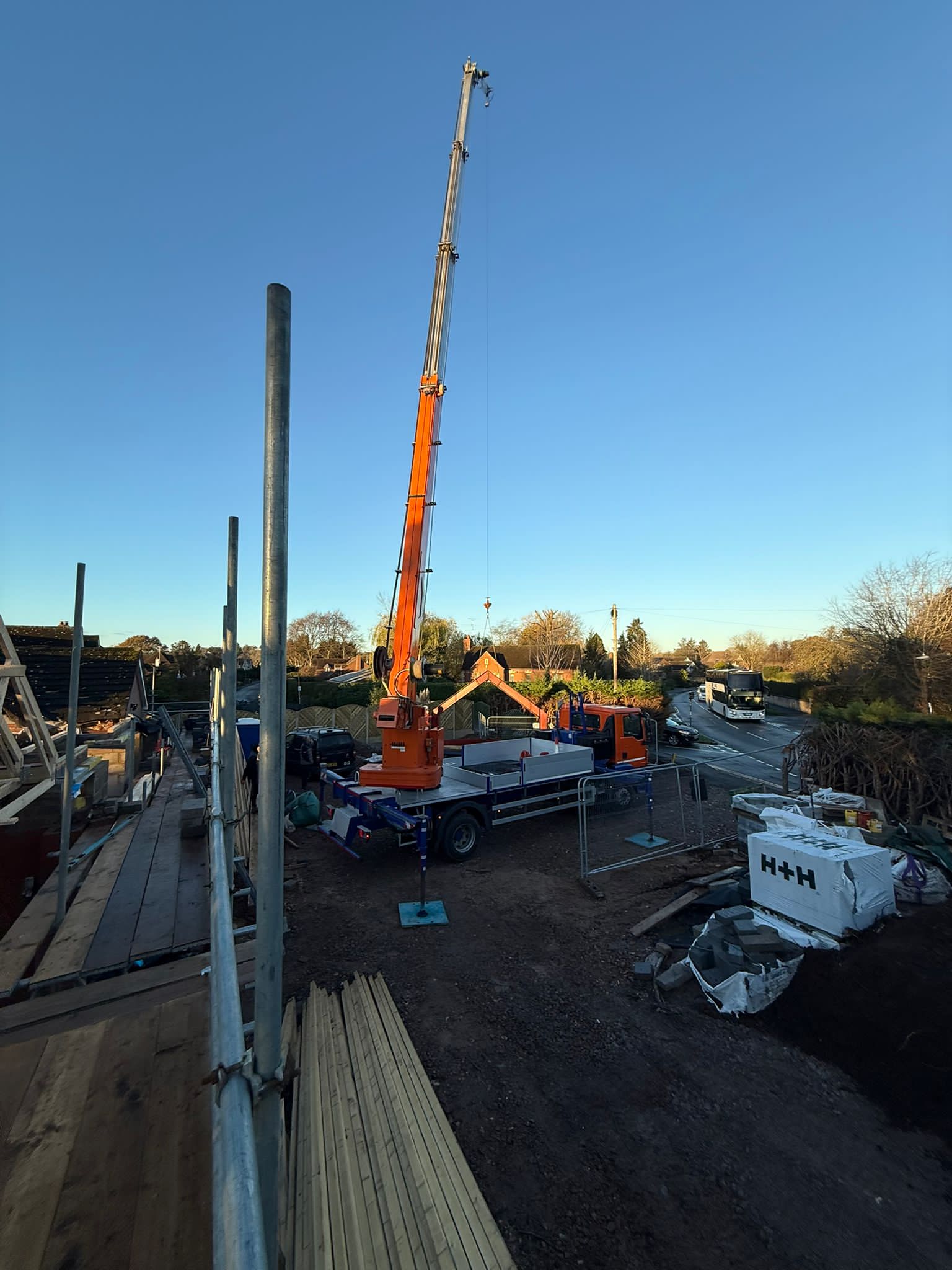 Crane on site lifting roof materials into position on a clear day.
