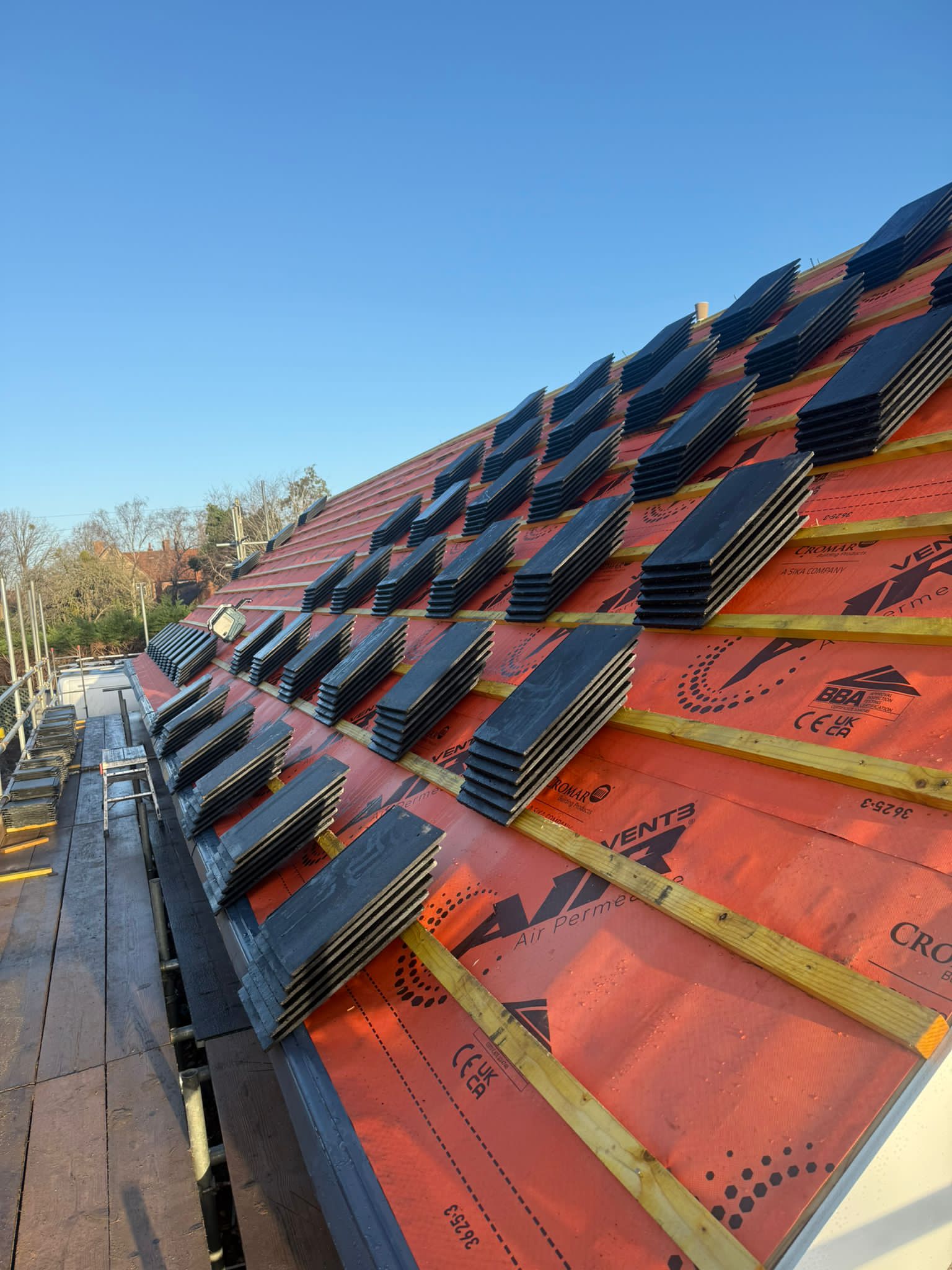 Stacks of slate laid out over orange membrane on a roof slope.