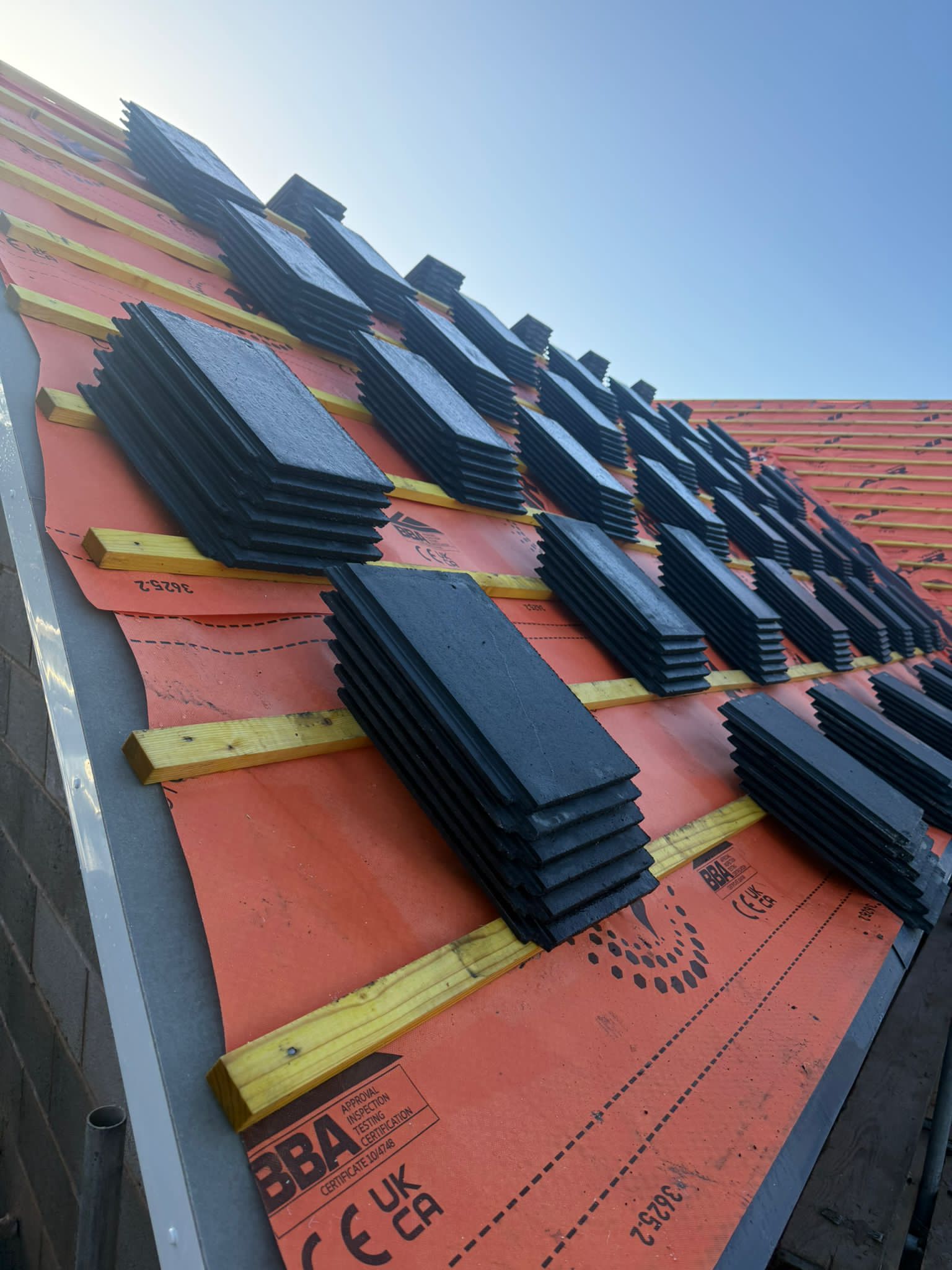 Stacked slates ready for installation on orange membrane with battens visible underneath.