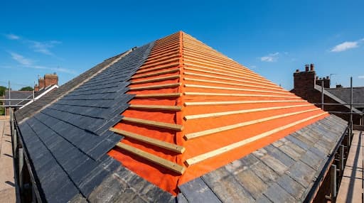 Fresh slate roof with bright orange breather membrane and timber battens under a clear blue sky.