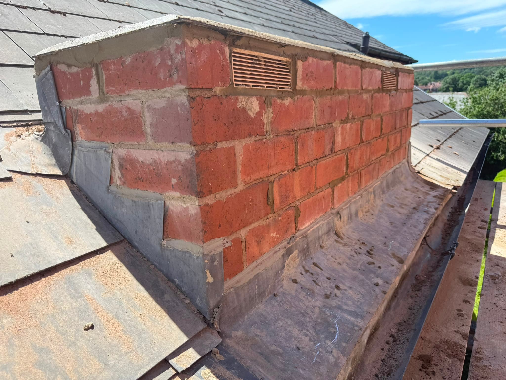 Finished capped brick chimney with air vents and fresh lead flashing dressed around the base.