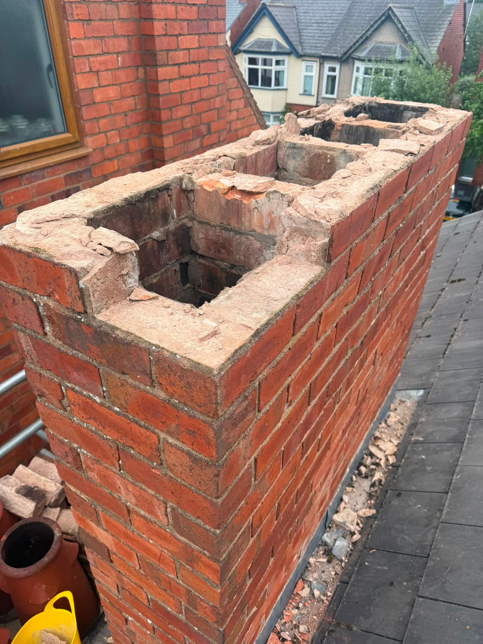 Old chimney stack partly taken down with the worn brickwork and open flues exposed, rubble on the roof.