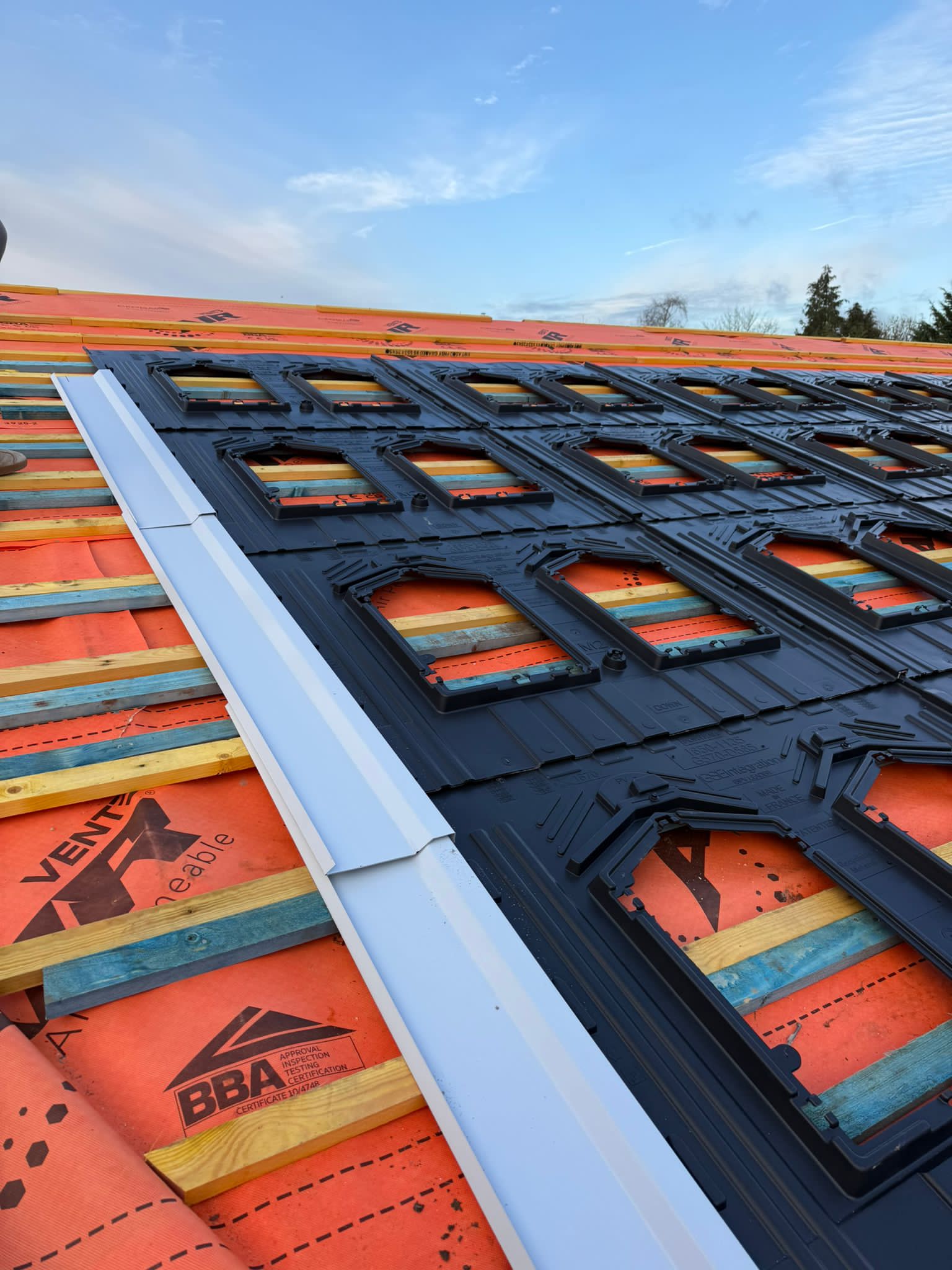 Close-up of a roof edge with bright membrane and neatly aligned slates being installed.