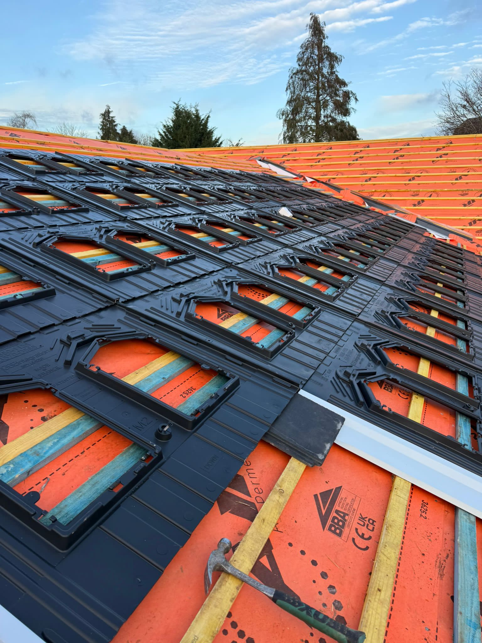 New slates lined up over orange breather membrane during a roof rebuild.
