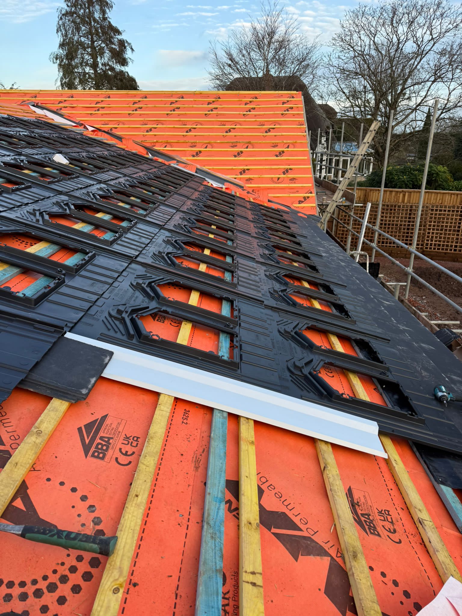 Fresh slate work being laid across orange breather membrane on a steep roof pitch.
