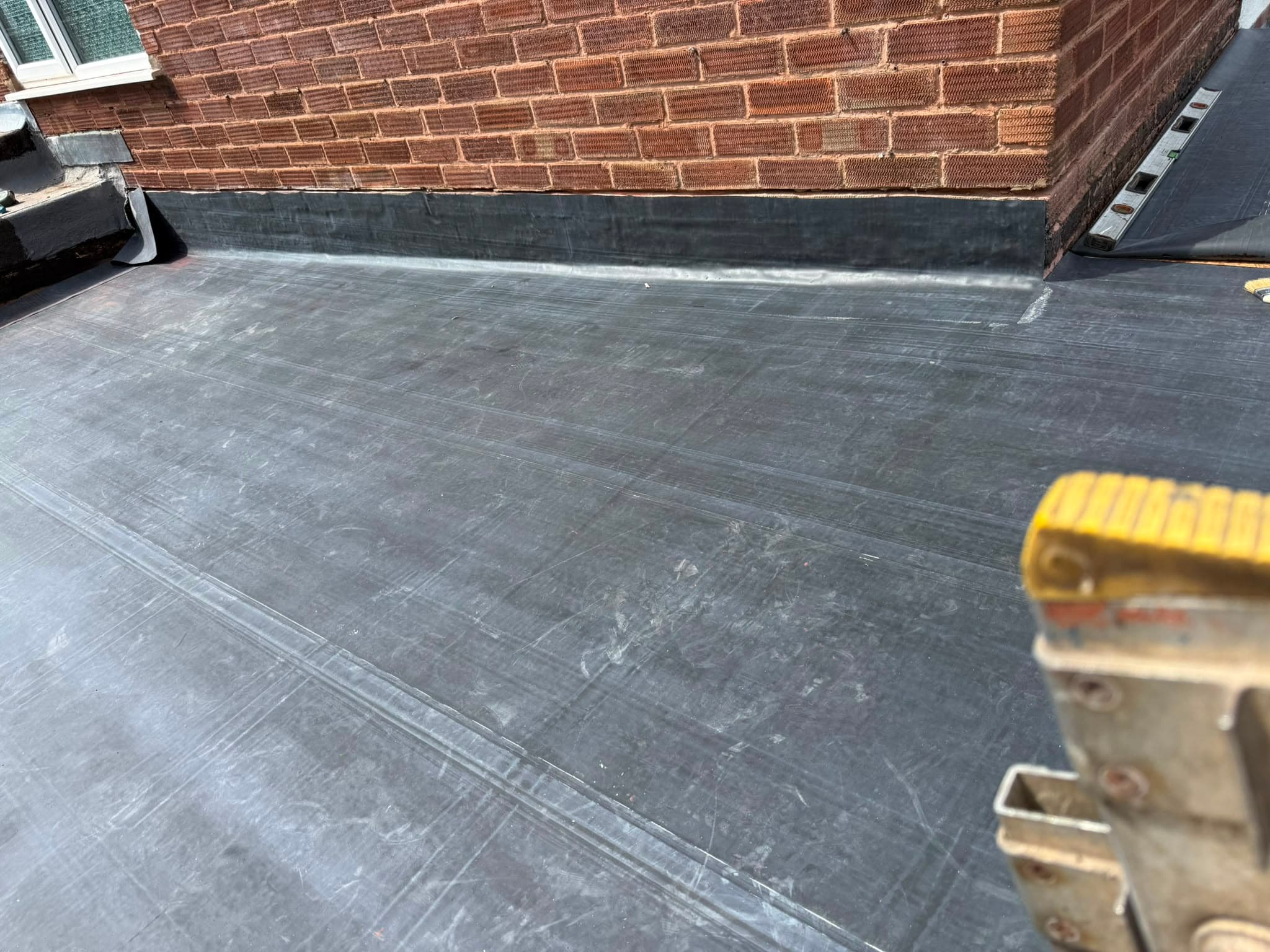 Black EPDM rubber membrane being laid on a flat roof and dressed up a brick wall part-way through the job.