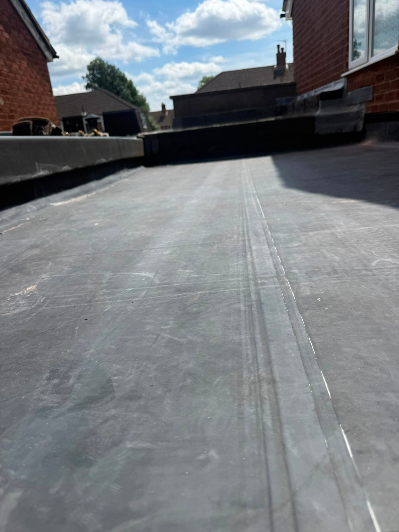 Finished black rubber flat roof running clean and flat to a neat edge trim under a clear blue sky.