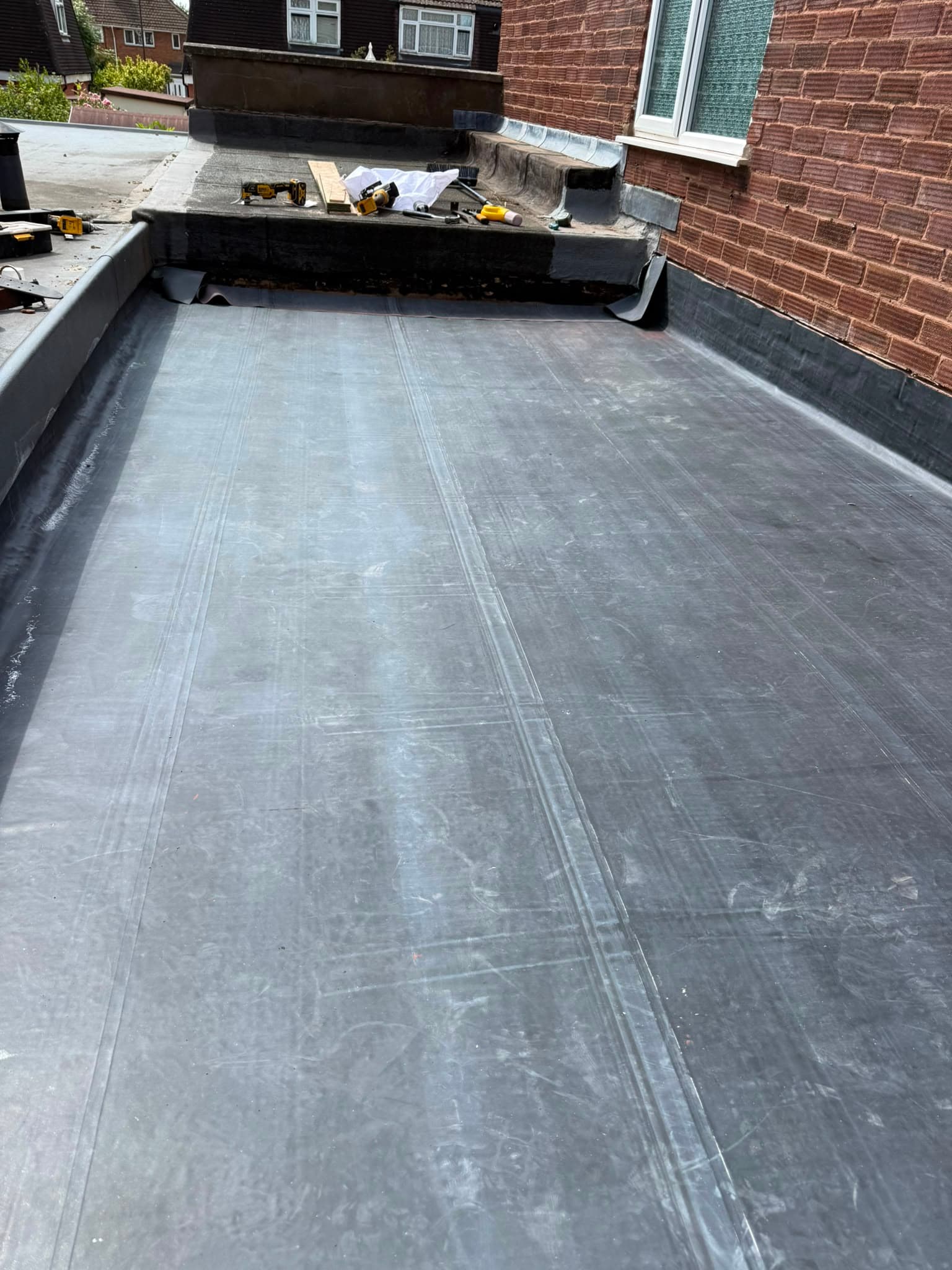 Completed black rubber flat roof laid wall to wall with a dressed upstand against a brick wall.