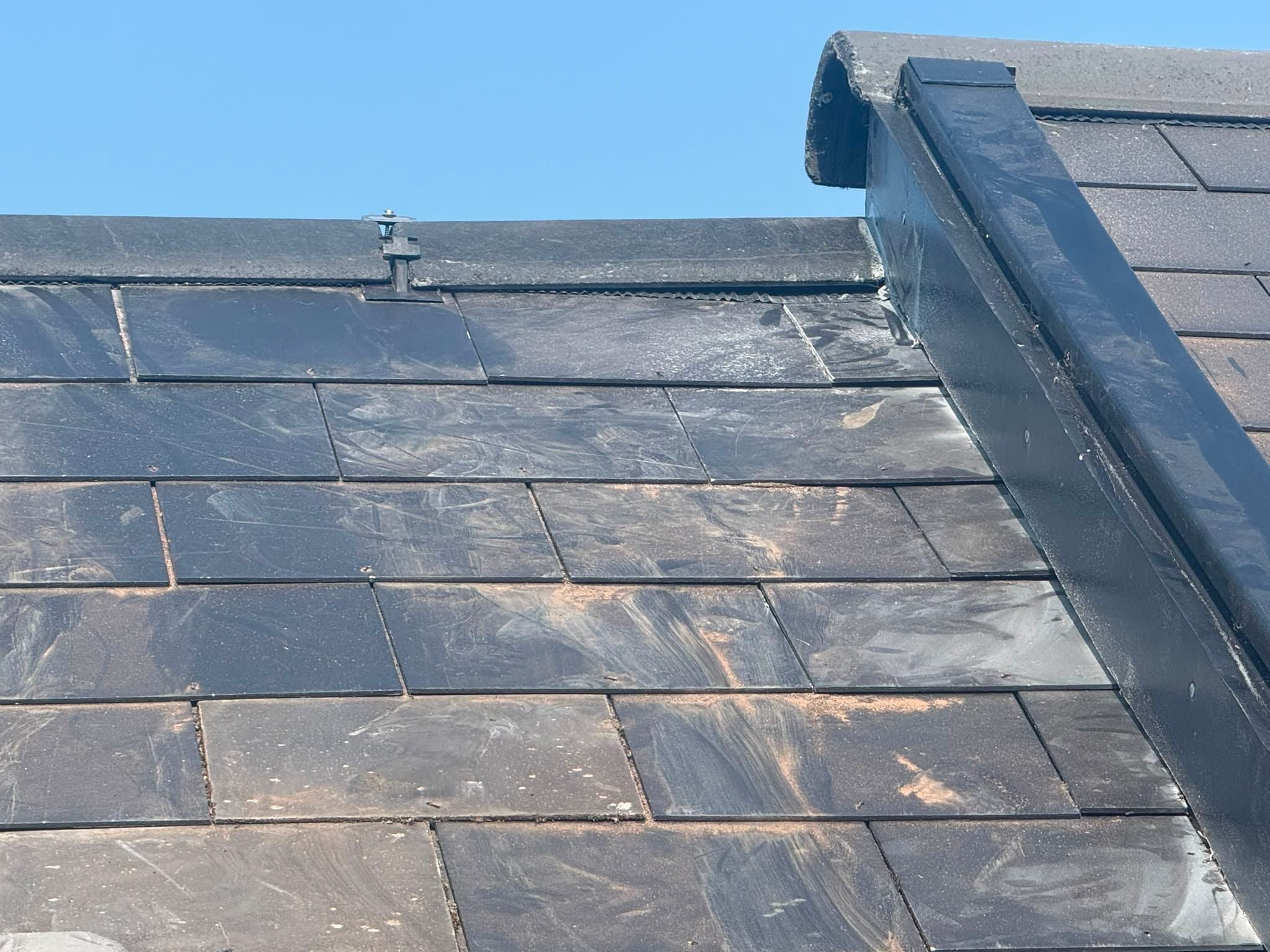 Tidy finished roof slope with fresh lead flashing dressed down the hip under a clear blue sky.