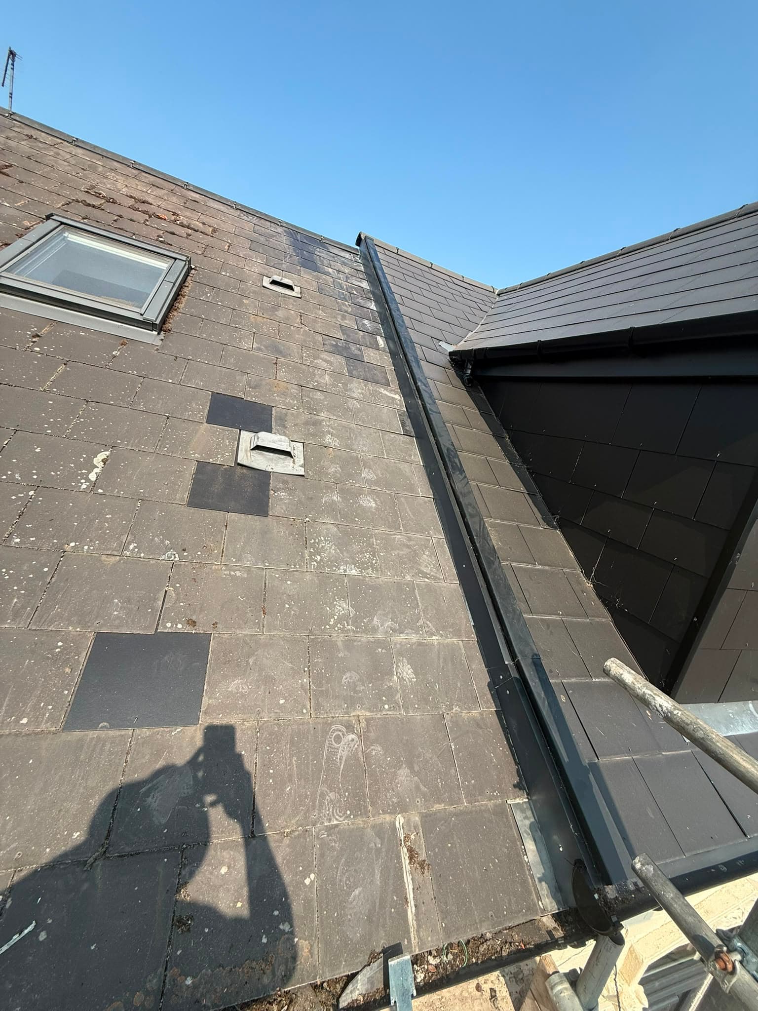 Repaired tiled roof section with replacement tiles meeting a neighbouring roof.